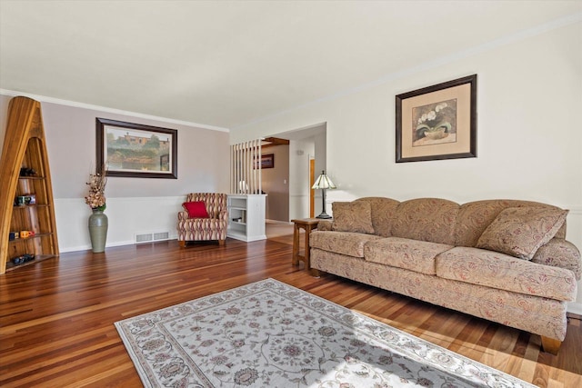 living area featuring visible vents, baseboards, wood finished floors, and ornamental molding