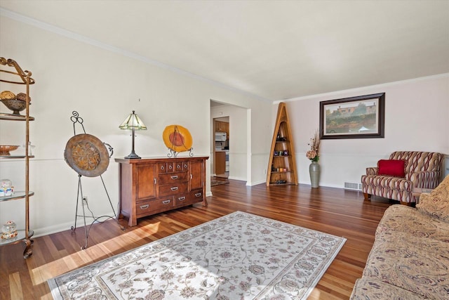 sitting room featuring visible vents, baseboards, wood finished floors, and ornamental molding