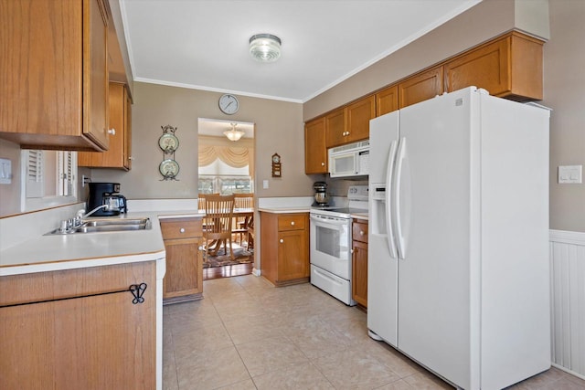 kitchen with white appliances, brown cabinetry, ornamental molding, a sink, and light countertops