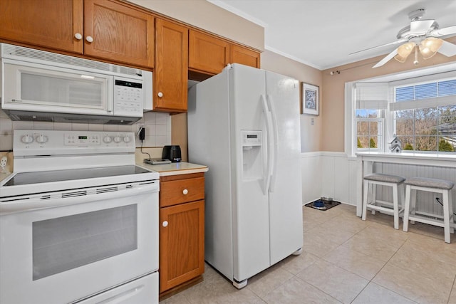 kitchen featuring white appliances, brown cabinets, light tile patterned flooring, and wainscoting