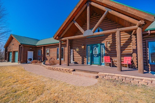 entrance to property featuring a porch, driveway, log exterior, and an attached garage