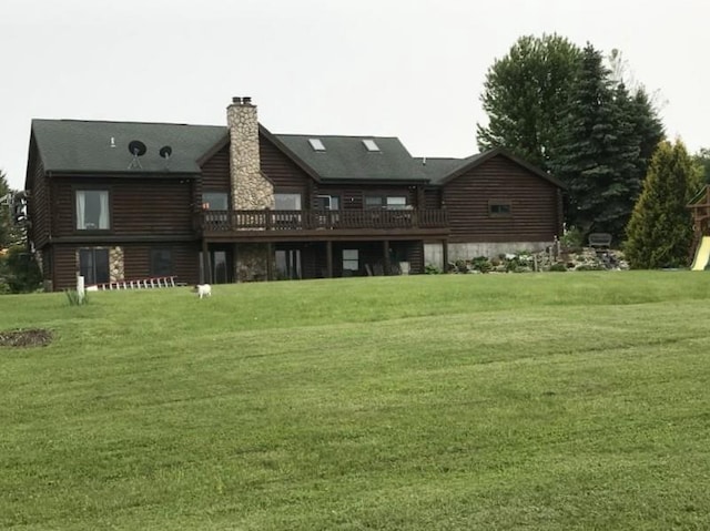 back of house with a deck, a chimney, log exterior, and a lawn