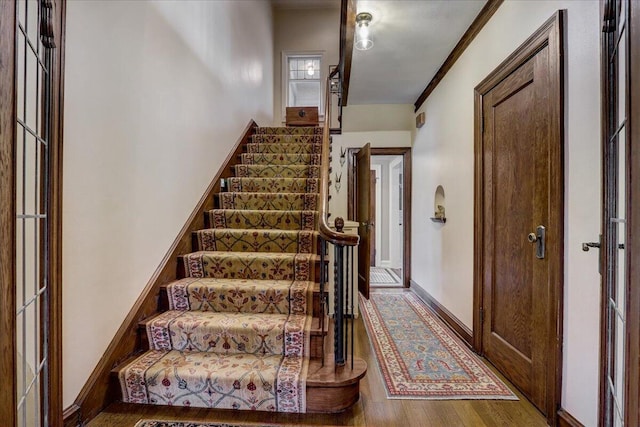 staircase featuring ornamental molding, wood finished floors, and baseboards