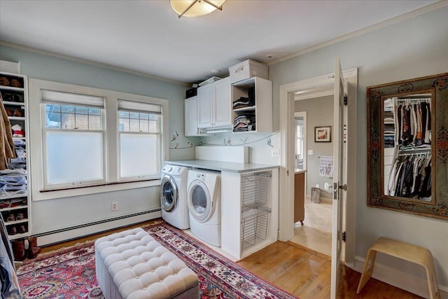 clothes washing area featuring a baseboard radiator, washing machine and dryer, cabinet space, light wood finished floors, and crown molding