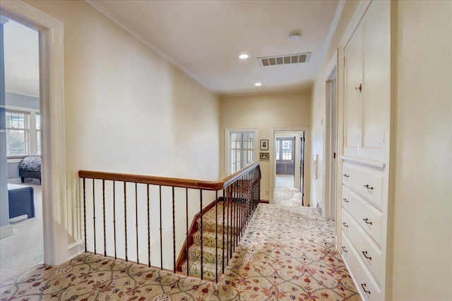 corridor featuring ornamental molding, visible vents, light carpet, and an upstairs landing