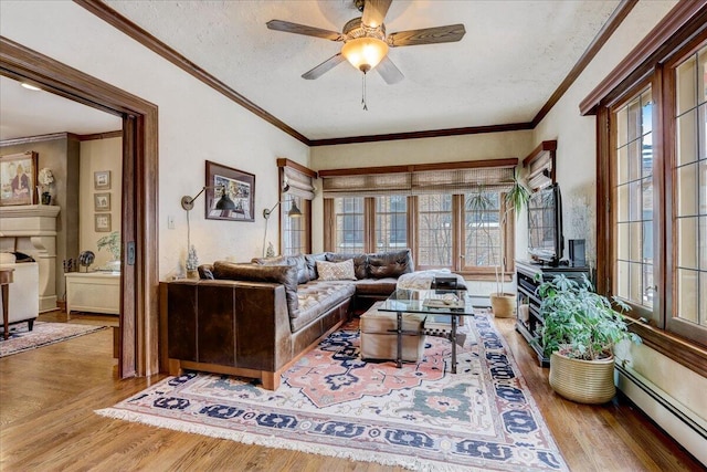 living room featuring a baseboard heating unit, crown molding, ceiling fan, and wood finished floors