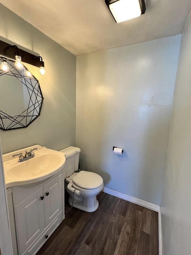 half bath with vanity, toilet, wood finished floors, and baseboards