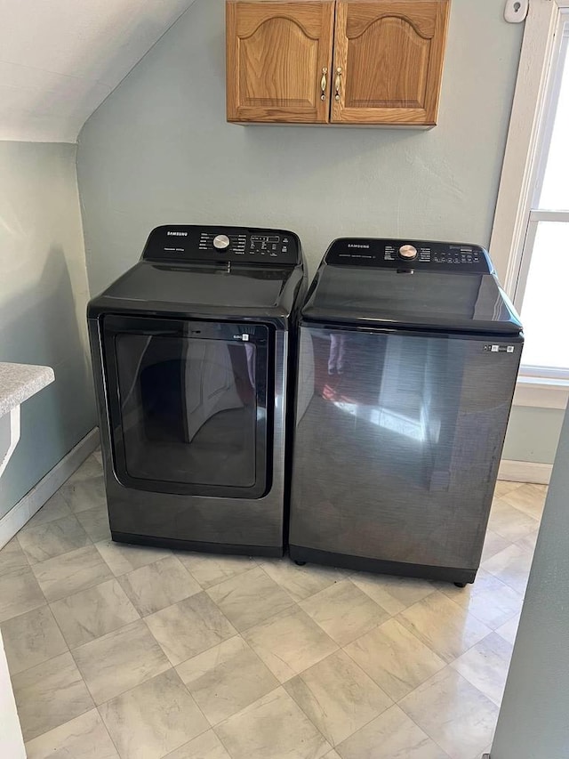 clothes washing area with washing machine and dryer, cabinet space, and baseboards