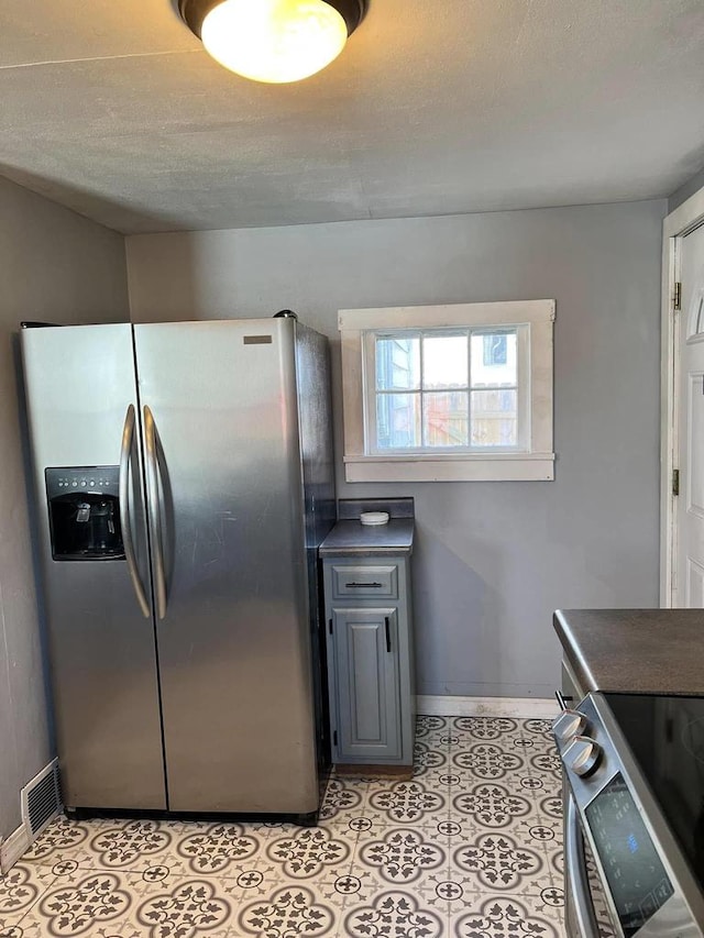 kitchen with dark countertops, a textured ceiling, appliances with stainless steel finishes, light tile patterned floors, and baseboards