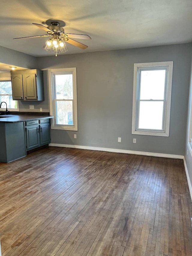 kitchen featuring dark wood-style floors, baseboards, a sink, stainless steel dishwasher, and dark countertops