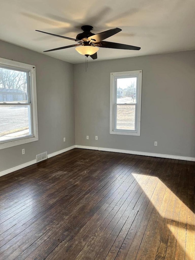 empty room featuring dark wood-type flooring, visible vents, a wealth of natural light, and ceiling fan