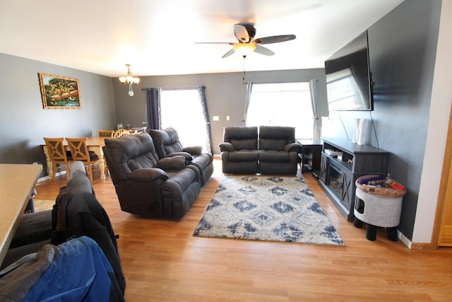 living room featuring baseboards, light wood finished floors, and ceiling fan with notable chandelier