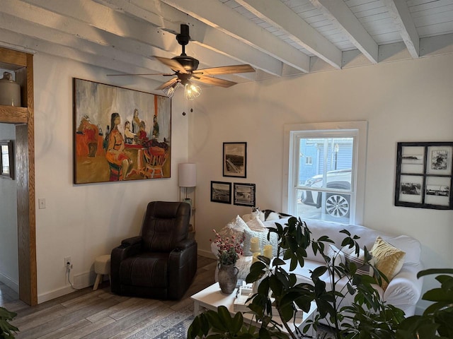 living area featuring a ceiling fan, beam ceiling, baseboards, and wood finished floors