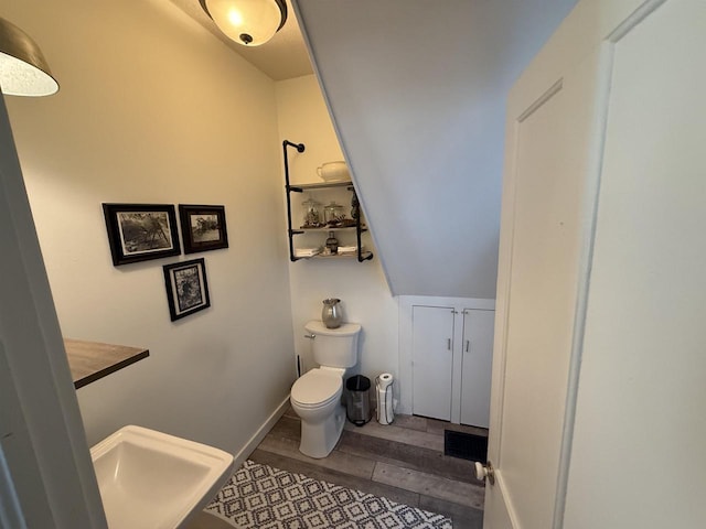 half bathroom featuring lofted ceiling, wood finished floors, toilet, and baseboards