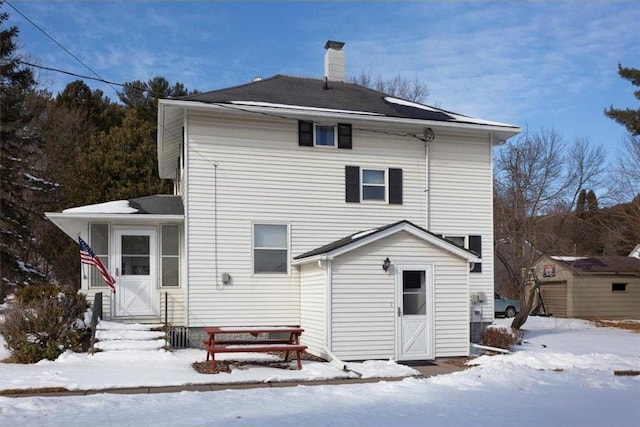 snow covered rear of property with a chimney