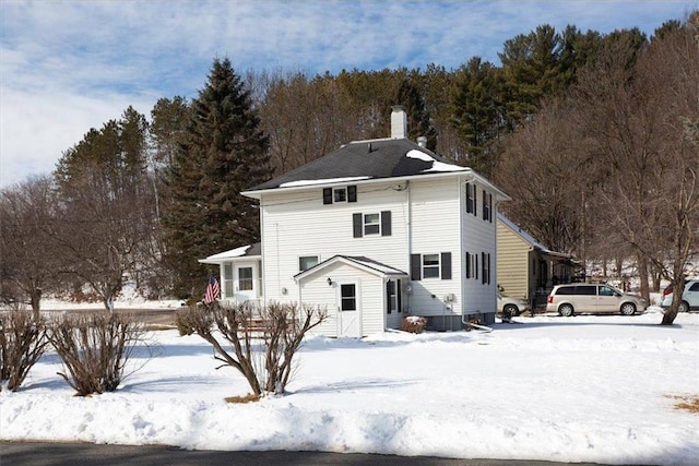 snow covered rear of property featuring a chimney