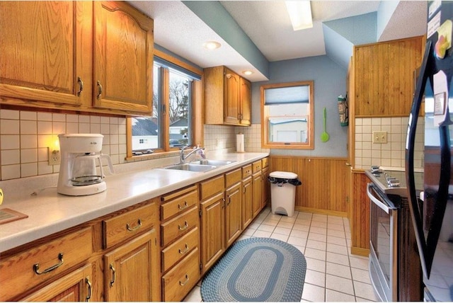 kitchen with light tile patterned floors, a wainscoted wall, a sink, light countertops, and brown cabinets