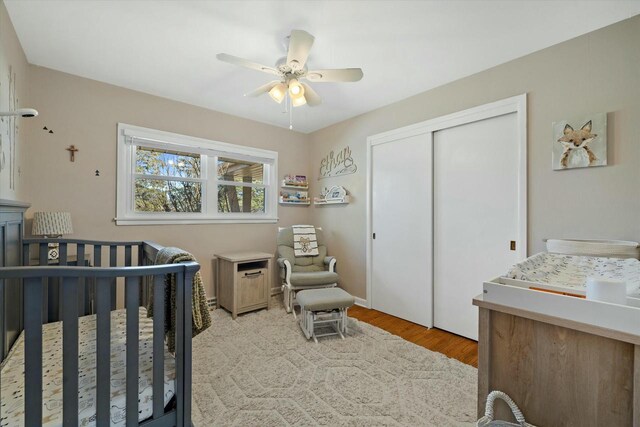 bedroom with light wood-type flooring, a closet, a crib, and a ceiling fan