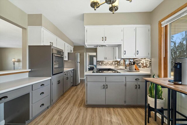 kitchen with gray cabinetry, a sink, appliances with stainless steel finishes, light countertops, and decorative backsplash