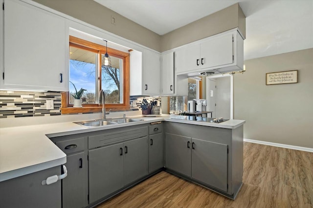 kitchen featuring wood finished floors, gray cabinetry, a sink, black electric cooktop, and backsplash