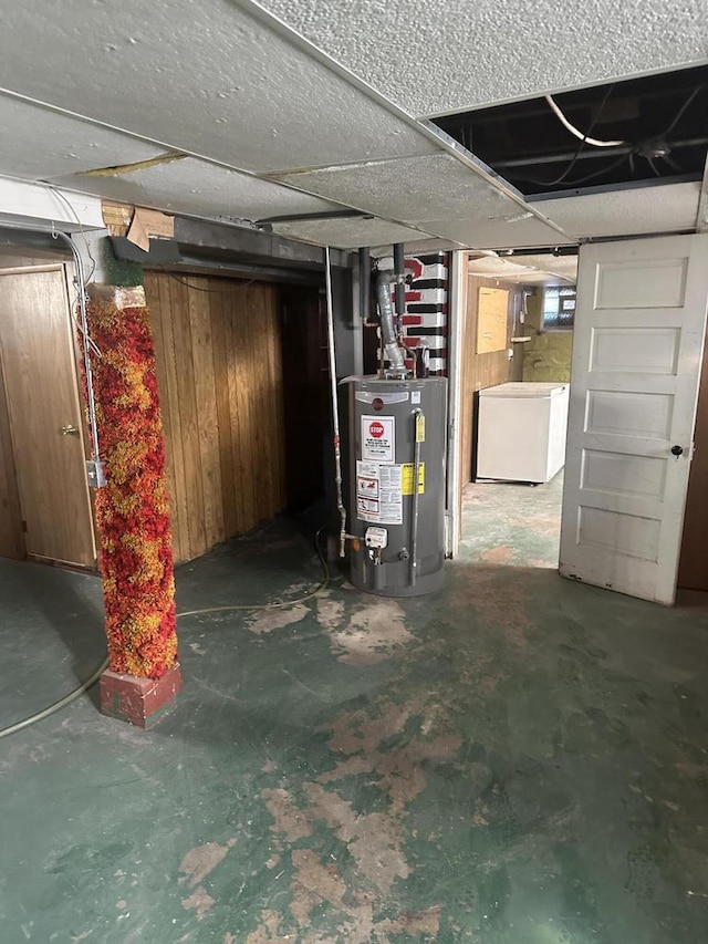 basement featuring water heater, wooden walls, and fridge