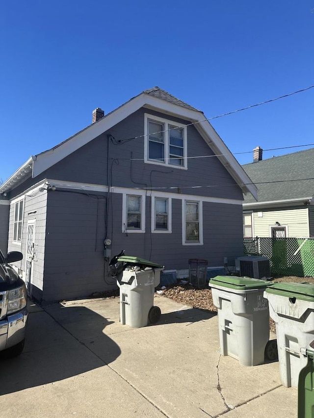 back of house featuring central air condition unit, a chimney, and fence