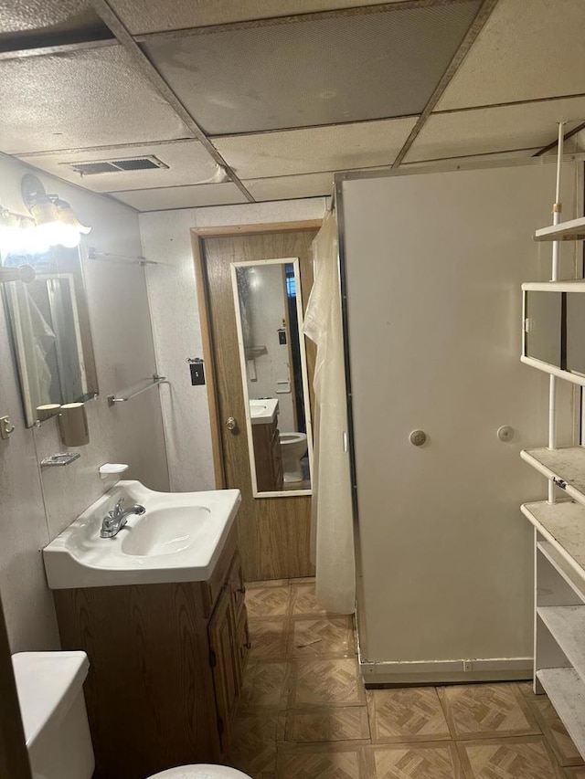 bathroom featuring visible vents, a drop ceiling, vanity, and toilet