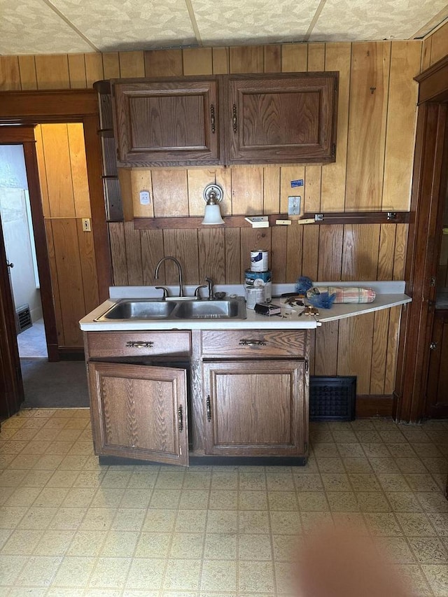 kitchen with wooden walls, a sink, visible vents, light countertops, and light floors