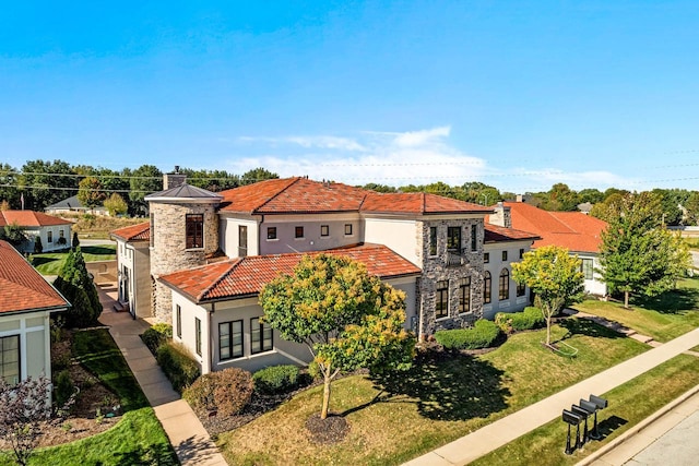 mediterranean / spanish-style home featuring stucco siding, a front lawn, stone siding, a chimney, and a tiled roof