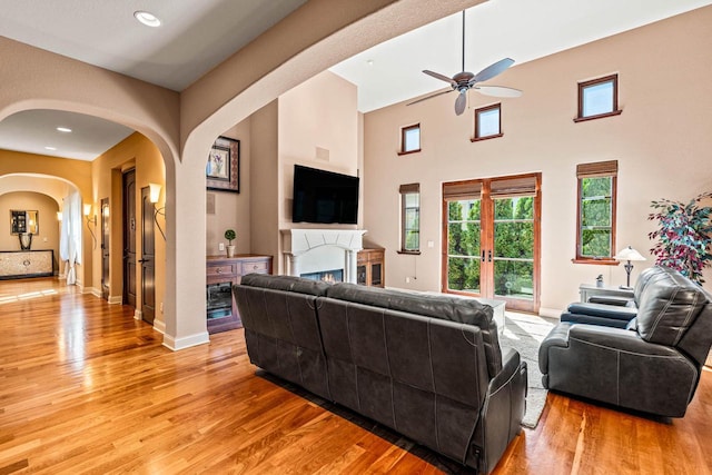 living area featuring light wood-style flooring, arched walkways, baseboards, and a lit fireplace