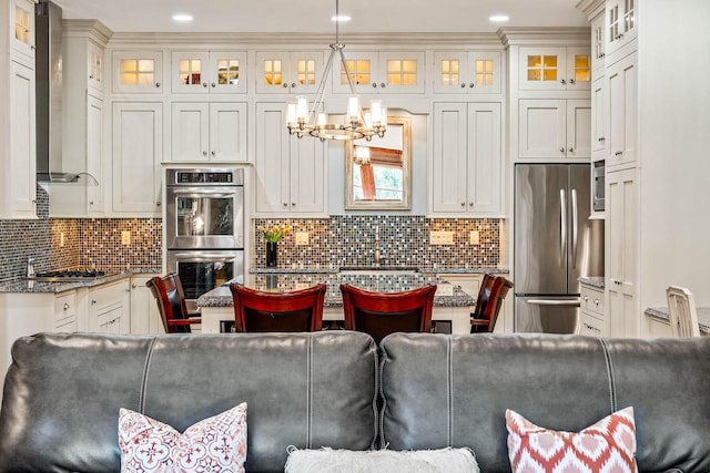 kitchen featuring hanging light fixtures, decorative backsplash, stainless steel appliances, and wall chimney exhaust hood