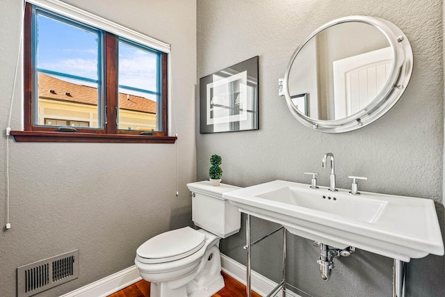 bathroom featuring visible vents, toilet, baseboards, and a textured wall