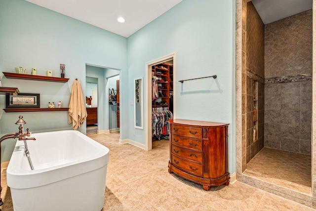 bathroom featuring a walk in closet, recessed lighting, baseboards, tiled shower, and a freestanding bath