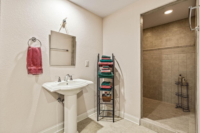 bathroom featuring tile patterned flooring, a sink, baseboards, and tiled shower