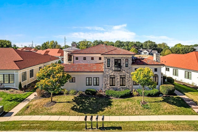 mediterranean / spanish home featuring stucco siding, a front lawn, stone siding, a tiled roof, and a residential view