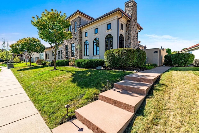 mediterranean / spanish house with stone siding, stucco siding, a chimney, and a front yard