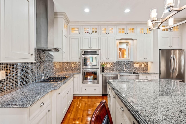 kitchen featuring a sink, light wood-style floors, appliances with stainless steel finishes, wall chimney exhaust hood, and decorative backsplash