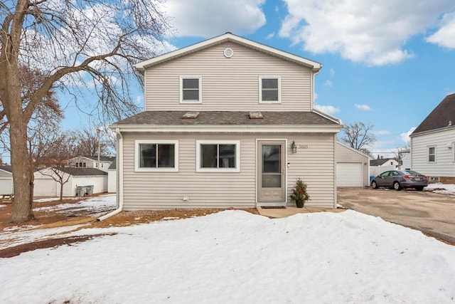 snow covered back of property with an outbuilding, roof with shingles, and a garage