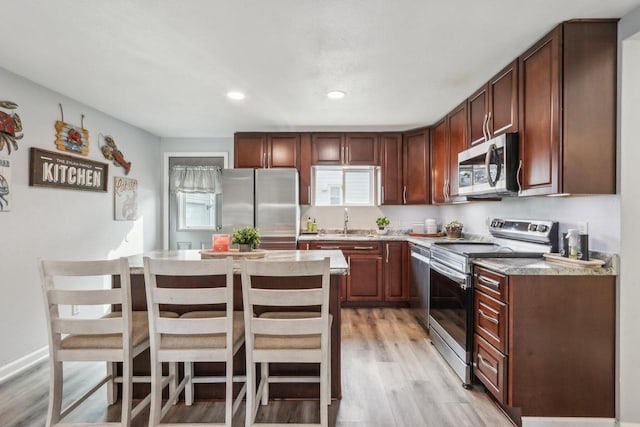 kitchen with light wood finished floors, a kitchen island, appliances with stainless steel finishes, a kitchen breakfast bar, and a sink