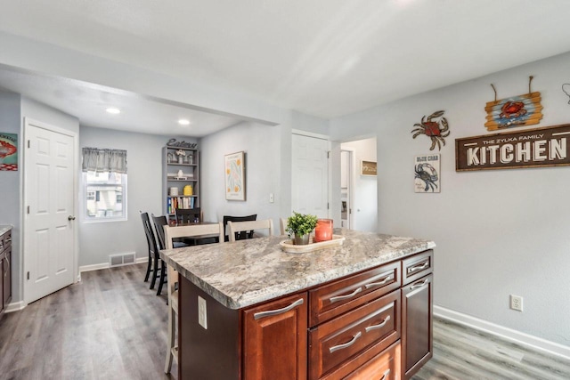 kitchen with light wood-style flooring, a center island, visible vents, and baseboards