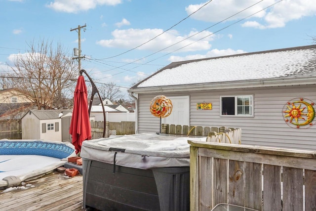 wooden deck with a hot tub, fence, a storage unit, and an outbuilding