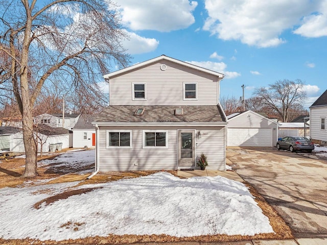 snow covered back of property with a garage, a shingled roof, and an outdoor structure