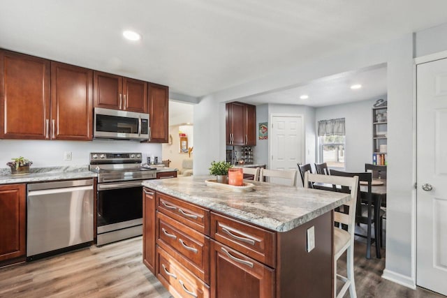 kitchen featuring a kitchen island, wood finished floors, stainless steel appliances, a kitchen bar, and recessed lighting