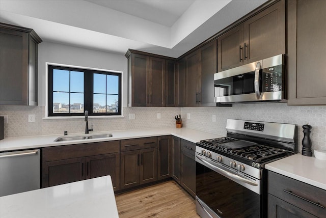 kitchen with appliances with stainless steel finishes, light countertops, a sink, and tasteful backsplash