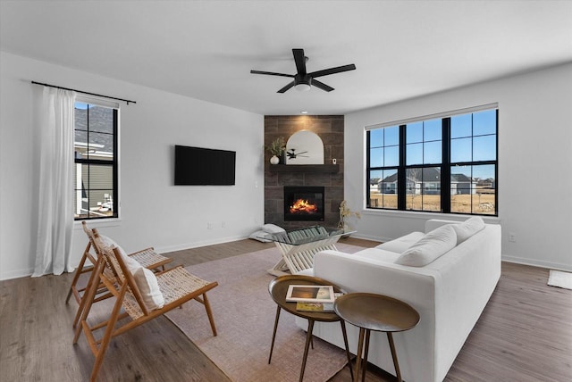 living area with baseboards, a fireplace, a ceiling fan, and wood finished floors