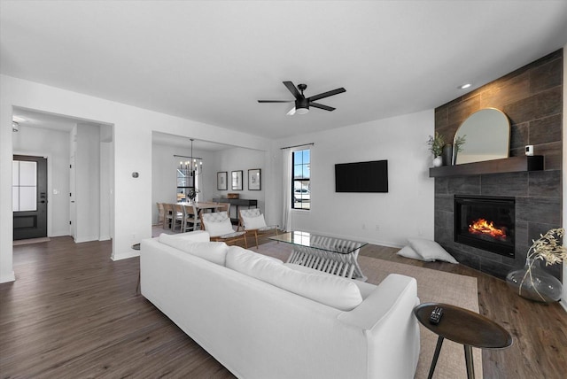 living area with dark wood-type flooring, a fireplace, baseboards, and ceiling fan with notable chandelier