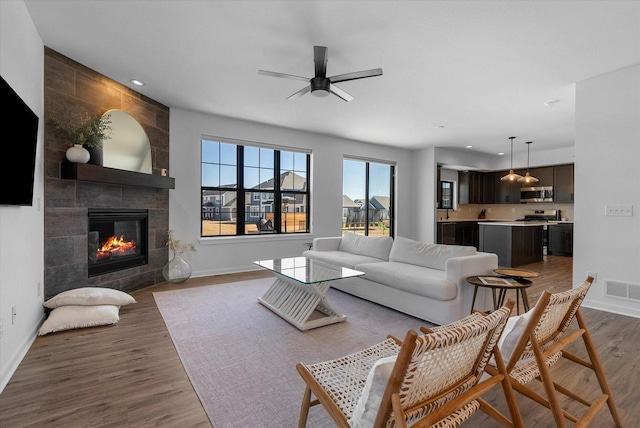 living room featuring a tile fireplace, recessed lighting, wood finished floors, visible vents, and baseboards