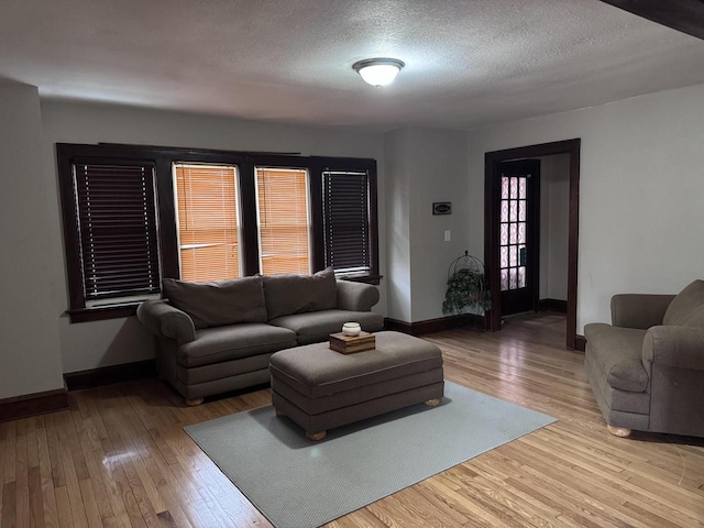 living area featuring a textured ceiling, wood-type flooring, and baseboards