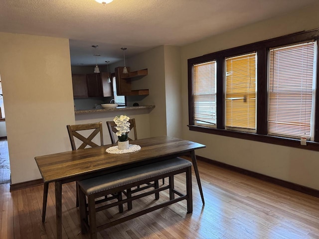 dining space with a textured ceiling, light wood-type flooring, and baseboards