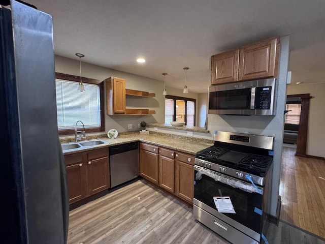 kitchen with stainless steel appliances, light wood-type flooring, a sink, and hanging light fixtures